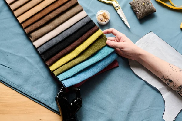 Close-up of hands of young woman with disability choosing fabric and colors for new sesonal fashion collection by workplace
