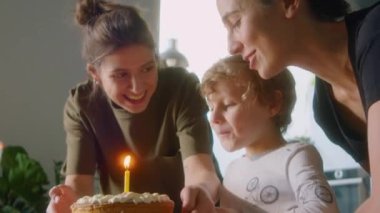 Mutlu lezbiyen anneler, doğum günü pastasında mum üflerken oğlunu öpüyor.