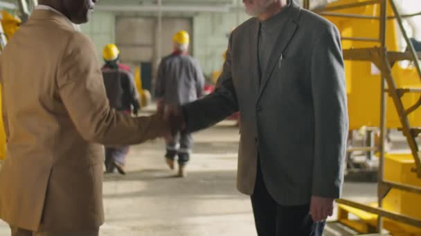 工場での作業中に会議しながら ハードハットと正式なスーツ握手で中年アフリカ系アメリカ人エンジニアのショットを傾け 白人の同僚と話す — ストック動画
