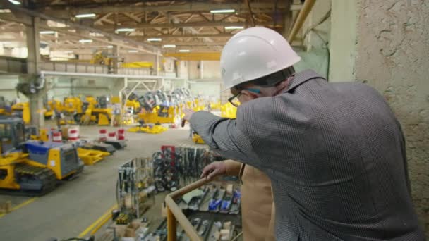 非洲裔美国工程师 头戴硬礼帽 穿着正装 站在工厂的上层 向白人同事解释生产过程 — 图库视频影像