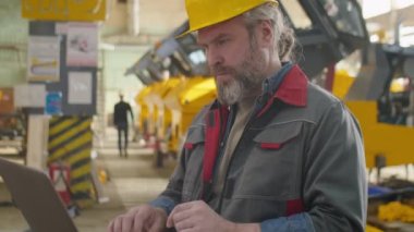 Makine fabrikasında dizüstü bilgisayar kullanan Kafkasyalı kıdemli işçi.