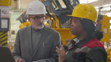 Genç Afro-Amerikan kadın mühendis fabrikada birlikte çalışırken üst düzey Kafkasyalı yöneticiye laptopta bir şey anlatıyor.