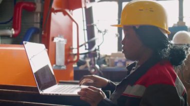 Makine fabrikasında duran ve dizüstü bilgisayar kullanan kadın bakım teknisyeni.