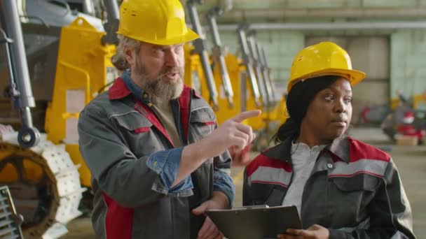 年轻的非洲裔美国女工程师 戴着硬帽 在机械厂一起工作时 在剪贴板上与白人高级同事讨论一些事情 — 图库视频影像