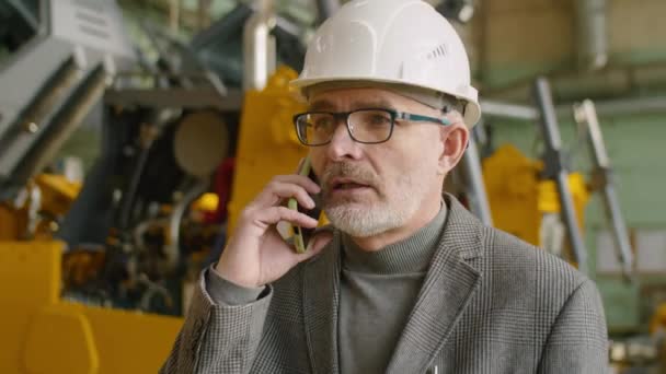 身穿正装 头戴硬礼帽的高级男性工程师在机械厂走来走去 用手机交谈 — 图库视频影像