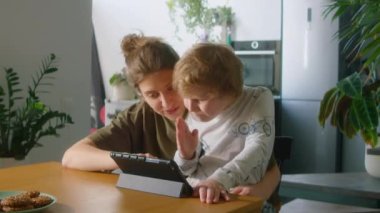 Heyecanlı anne ve küçük oğlunun evde oturup dijital tabletle oynayıp kazanırken kollarını kaldırarak bağırışlarını yakınlaştır.
