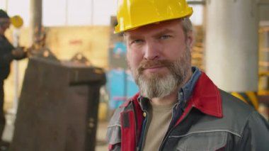 Fabrikada iş günü kameraya çekilen kasketli ve üniformalı olgun erkek işçinin portresi.
