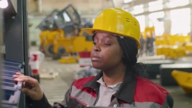 Fabrika deposundaki raflarda dijital tablet kullanan, kasklı Afrikalı Amerikalı kadın denetçi.