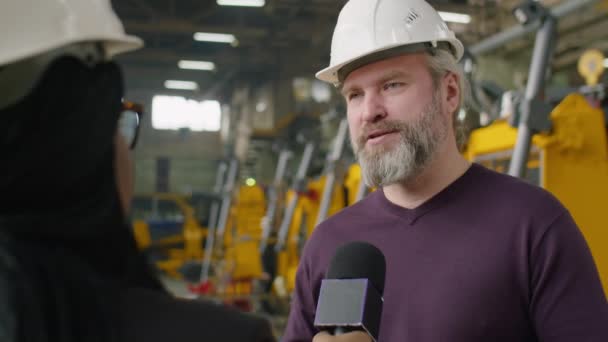 在接受电视记者有关重型设备制造厂的采访时 戴着硬礼帽的资深男性工程师一边对着话筒一边拍了照 — 图库视频影像