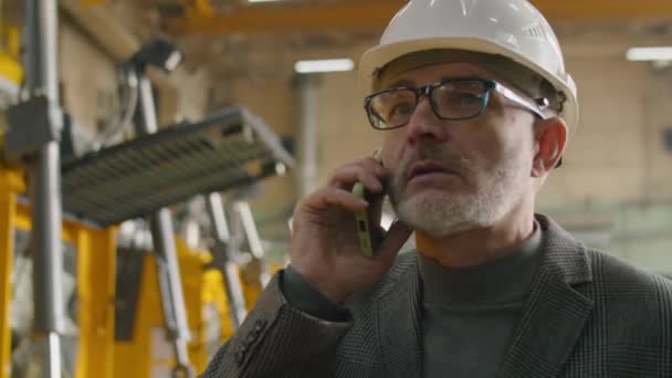 机械制造厂的高级男工程师 穿着正装 头戴安全帽 在手机上讲话 — 图库视频影像