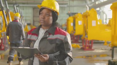 Genç Afrika kökenli Amerikalı kadın mühendis. Panodaki kağıtları inceliyor ve endüstriyel fabrikada çalışırken makinelere bakıyor.