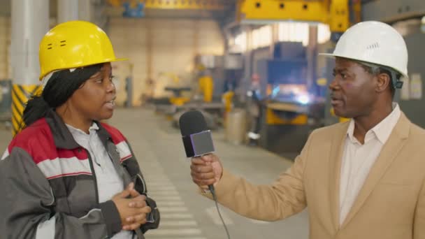 在机械厂接受电视记者采访时 戴着硬礼帽 身穿制服 手持话筒说话的非洲裔美国女工 — 图库视频影像