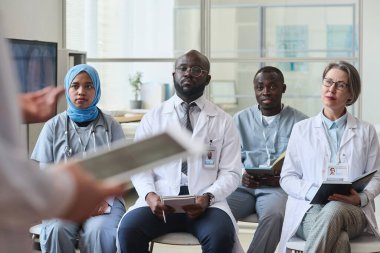 Konuşmacıları dinleyen ve ofisteki tıp seminerinde notlar alan bir grup ciddi doktor.