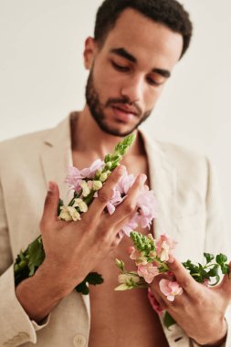 Ceketli genç sakallı adam beyaz arka planda izole edilmiş güzel çiçeklerle ellerine bakıyor.