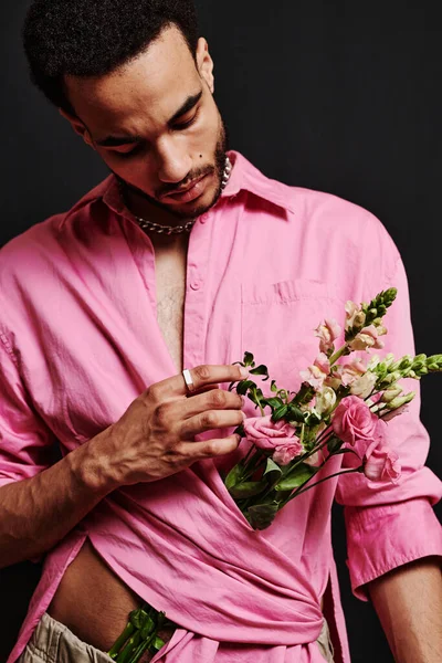 Young sensual man touching beautiful bouquet of flowers inside of his pink shirt