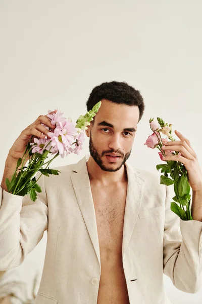 stock image Portrait of young bearded man looking at camera with bouquets of flowers in sleeves of his jacket isolated on white background