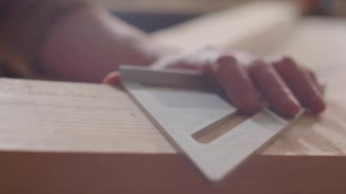 Marangozun elleri, tahta üzerine çizgi çizerken metal kare ve kalem kullanarak yakın çekim.