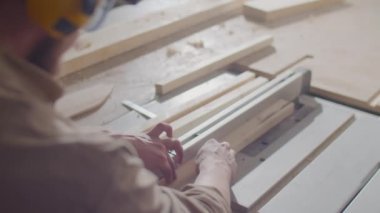 Marangozluk atölyesinde çalışırken masa testeresiyle tahta kesen güvenlik kulaklığı ve gözlüklü profesyonel marangoz.