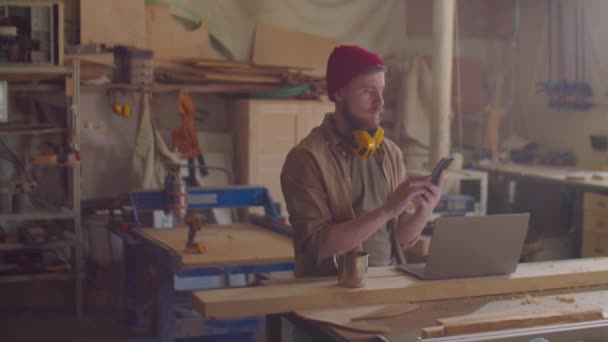 Jonge Mannelijke Houtbewerker Met Veiligheidsoorkappen Zijn Nek Met Smartphone Timmerwerkplaats — Stockvideo