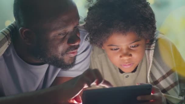 Alegre Niño Afroamericano Jugando Tableta Digital Con Padre Mientras Yacen — Vídeos de Stock