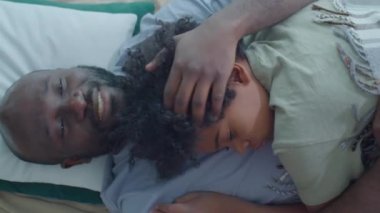 Afrika kökenli Amerikalı babayı severken, gülümseyen, kucaklayan ve kucaklayan küçük oğlu yatakta birlikte yatarken göğsünde uyurken.