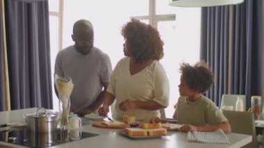 Babası etrafta dolaşıp onlarla konuşurken Afrikalı Amerikalı anne ve küçük oğlu evde aile kahvaltısı için sandviç hazırlıyorlar.