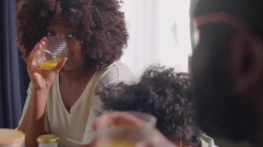 Afro-Amerikan kadın portakal suyu içiyor ve aile kahvaltısında oğlunun yanında otururken kocasıyla konuşuyor.