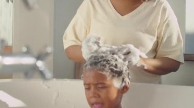 Afro-Amerikan bir annenin banyoda şampuanlı çocuk saçlarını yıkarkenki görüntüsü.