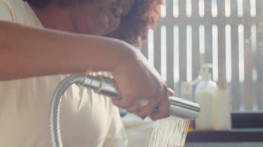 Annesi kafasını suyla yıkarken küçük Afrikalı Amerikalı çocuk banyoda oturuyor.