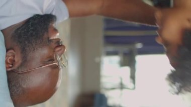 Mutlu Afrikalı Amerikalı babanın dikey çekimleri. Sırtüstü uzanmış, neşeli küçük oğlunu kucaklıyor ve onunla evde oynarken burunlarını sürtüyor.