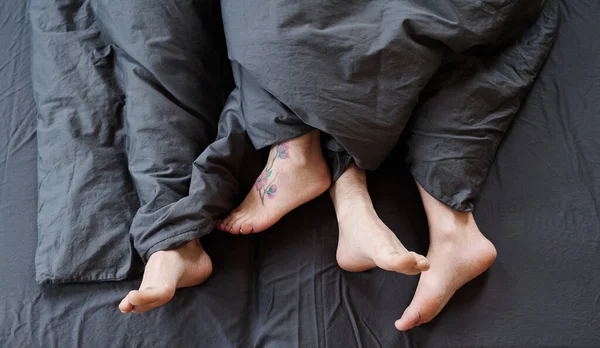 トップダウンショットの現代的な認識できないロマンチックなカップルの足ベッドで発見で朝 グレーベッドリネン — ストック写真