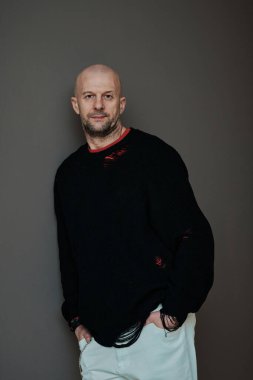 Dikey stüdyo portresi. Yakışıklı, olgun, günlük kıyafetler giyen, kameraya bakan, gri arka planda beyaz bir adam.