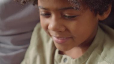 Sevgili babasıyla oturan, dijital tablette bir şeyler seyreden ve gülümseyen sevimli Afrikalı Amerikalı çocuğun el kamerasıyla çekilmiş yakın çekim görüntüleri.
