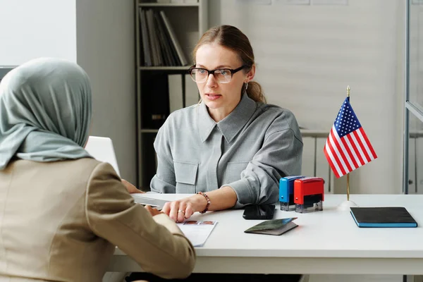 stock image Modern Caucasian consular officer sitting at desk in front of Muslim woman explaining her how to fill in application form