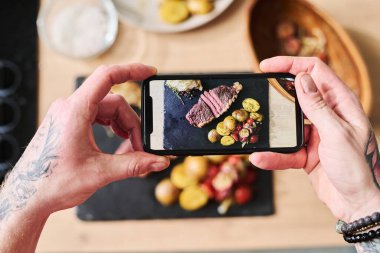 Yukarıdan aşağıya seçici odaklı yakın plan çekimde blogcu, akıllı telefon kamerasında ekmekli ve sebzeli bifteğin fotoğraflarını çekiyor.