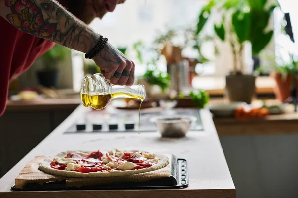 Молодой Бородатый Мужчина Готовит Пиццу Кухне Дома Добавляя Немного Оливкового — стоковое фото