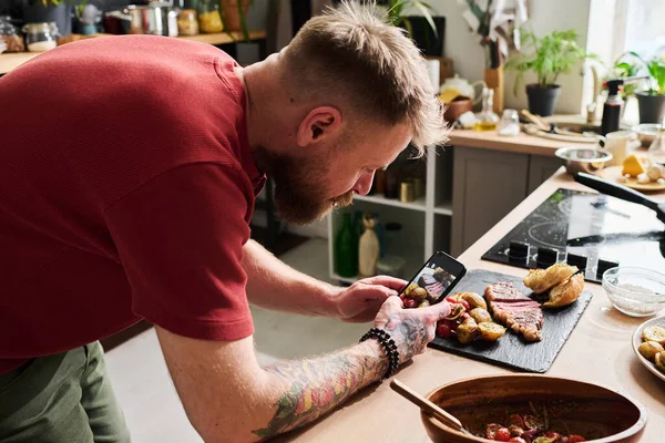 現代の男性食品ブロガーは ジャガイモとパンと牛肉のステーキの写真を撮るためにスマートフォンを使用して — ストック写真