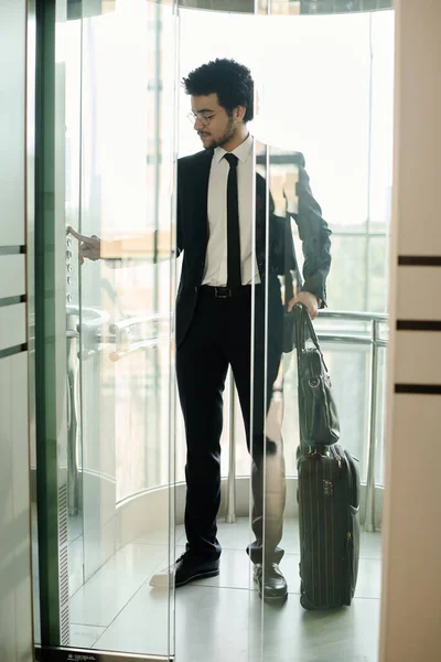 エレベーターの中に荷物を積んでボタンを押すだけでスーツ姿の若いビジネスマンが — ストック写真