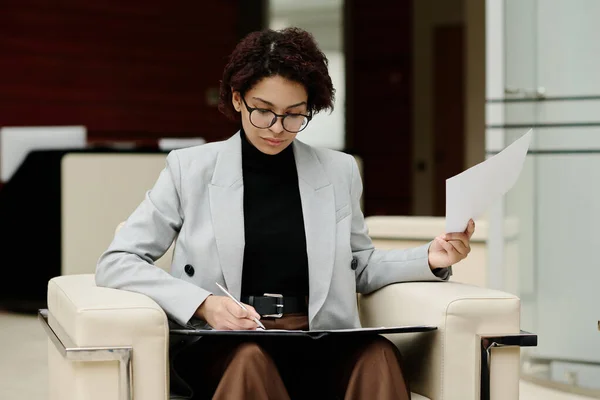 Młoda Bizneswoman Okularach Siedząca Fotelu Podpisująca Dokumenty Służbowe Biurze — Zdjęcie stockowe