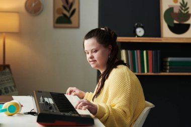 Down sendromlu modern beyaz kız portresi evde elektronik piyano çalarak vakit geçiriyor.