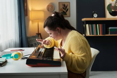 Down sendromlu genç beyaz kadın evde boş vakitlerini elektronik piyano çalarak ses efektleri seçerek geçiriyor.