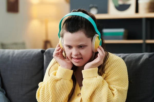 白种人快乐年轻女性唐氏综合征的画像 头戴耳机坐在客厅沙发上听最喜欢的歌曲 — 图库照片