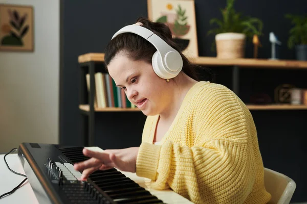 现代白人妇女与唐氏综合征穿着休闲装和耳机调整电子键盘的声音设置 — 图库照片