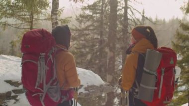 Sırt çantaları ve yürüyüş direkleriyle dağlarda yan yana duran ve kışın manzarasını tartışan turist çiftlerin arka planı.