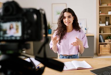 Genç beyaz kadın kameranın önünde oturmuş konu hakkında konuşurken blog için video kaydediyor.