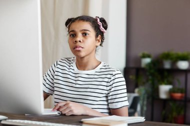Uzaktan eğitim sırasında bilgisayar başında otururken online toplantıya konsantre olan ciddi bir Afrikalı kız.
