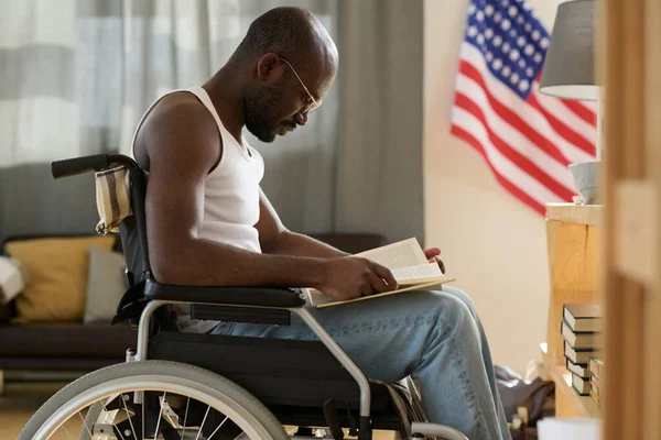 アフリカ系アメリカ人の男性が部屋の車椅子に座って情熱を持って本を読んで — ストック写真