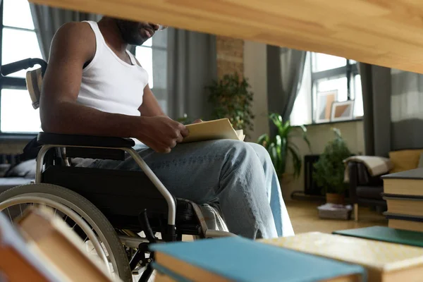 Крупный План Афроамериканца Сидящего Инвалидной Коляске Читающего Книгу Возле Стола — стоковое фото