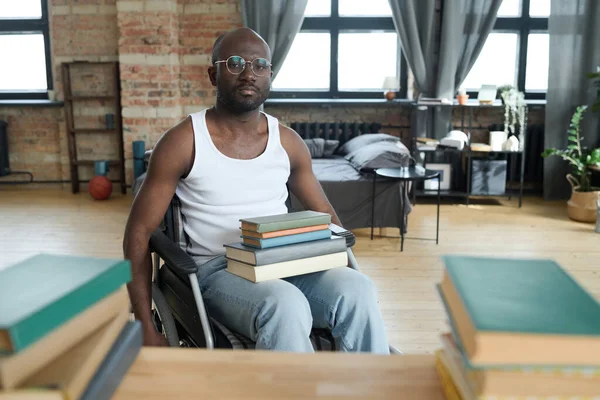 アフリカ系アメリカ人の男性の肖像画車椅子に座って膝の上に本を積みカメラを見て — ストック写真