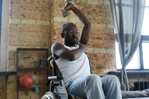 スポーツトレーニング中に車椅子に座っている間 アフリカの若い男は片手でダンベルを持ち上げる — ストック写真
